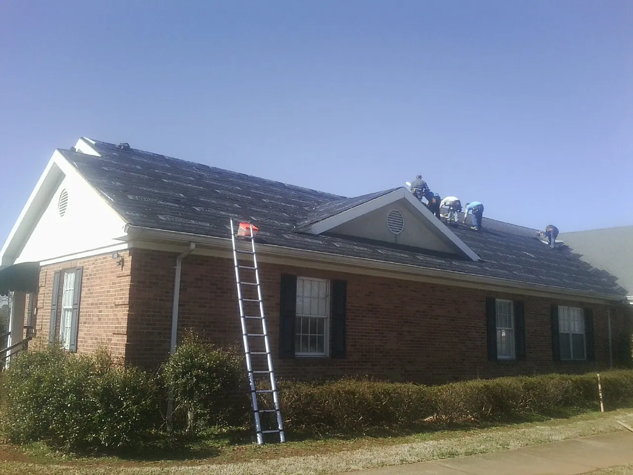 Crew tearing shingles off a brick ranch roof with a ladder set — Emergency Roof Repair work by our crew in Hereford