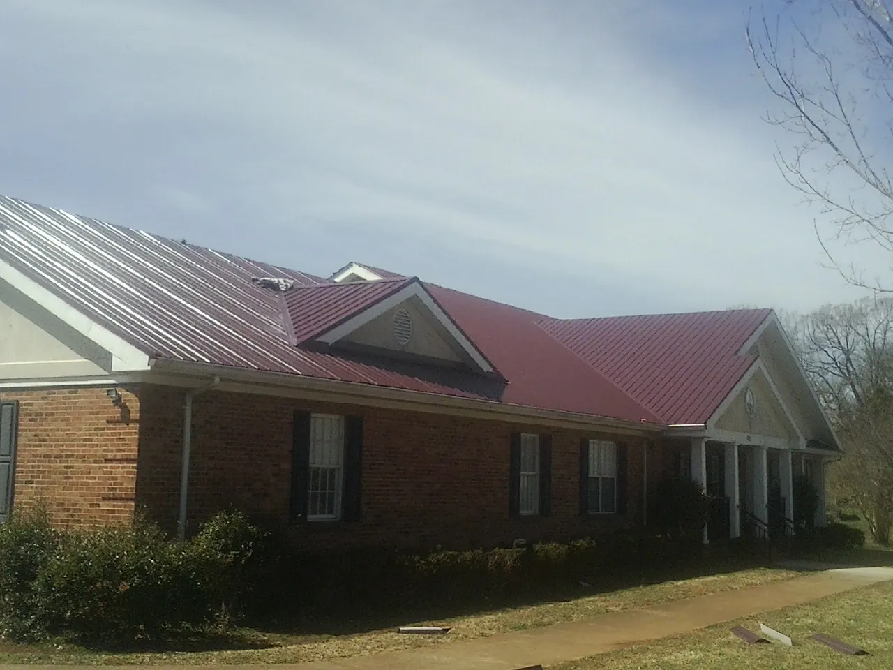 Red metal roof with gabled entries on a long brick building, from a Hail Damage Roof Repair job in Hereford