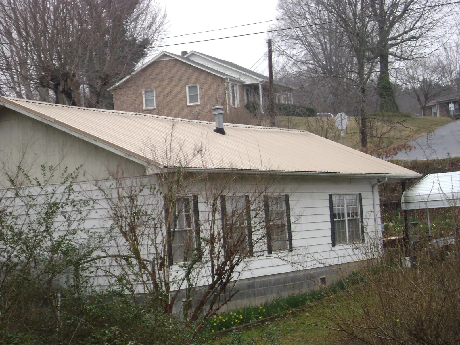 Tan metal roof on a white sided house set into a hillside — Commercial Roofing by Roofing Brothers in Hereford